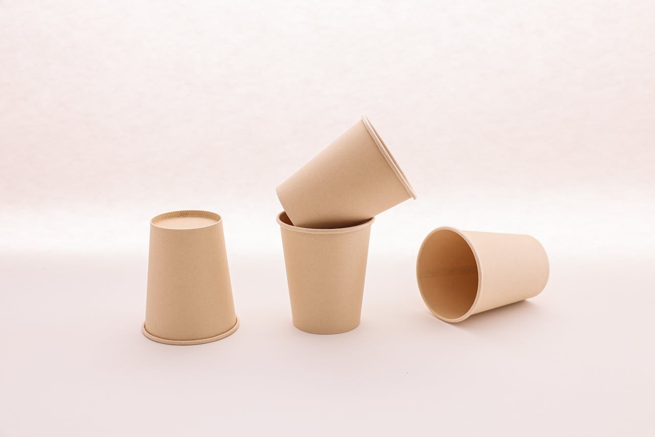 Four brown disposable paper cups arranged on a white surface. Ideal for eco-friendly concepts.